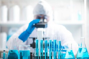 A scientist looks through a microscope while laboratory glass sits in front of him.